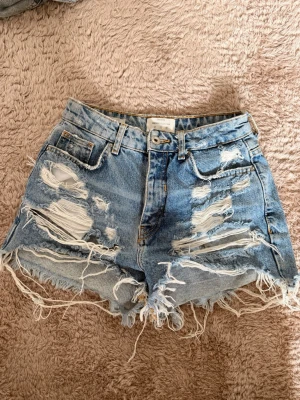Blåa jeansshorts från Bershka - Säljer ett par blåa jeansshorts från Bershka Vintage Collection. De är högmidjade med rejält slitna detaljer och fransig kant nertill. Storlek 36 men skulle säga att de är rätt små i storleken och passar bättre på någon som vanligtvis har 34 🤩