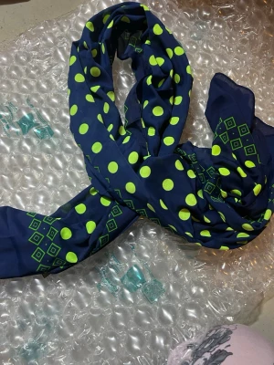 Blå scarf med limegröna prickar - Snygg blå scarf med limegröna prickar och grafiska mönster i hörnen. Tunn och lätt i materialet, perfekt att knyta runt halsen eller i håret för en färgklick till din outfit.