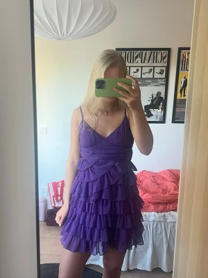 Lila volangklänning med snörning - Superfin lila kortklänning med volanger och smala axelband💜 Klänningen har omlott-detalj framtill och snörning i ryggen för en snygg passform. Tillverkad i ett lätt och luftigt material perfekt på sommaren! Materialet är polyester.