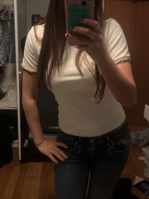 Vit ribbad topp med volangkant - Snygg vit topp med korta ärmar och volangkant vid ärmslut och nederkant. Modellen är figurnära och ribbad vilket ger en trendig och bekväm look.  Den har en jätte liten smink fläck om man kollar noga, men syns bara i vissa ljus och inget man tänker på. Annars har jag använt den 1 gång så vet inte hur de hamnat där 