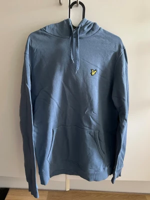 Blå hoodie från Lyle & Scott - Blå hoodie från Lyle & Scott med klassisk gul logga på bröstet. 
