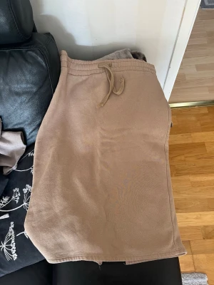 Beige sweatshirtkjol med snörning - En beige kjol i sweatshirtmaterial med snörning i midjan och slits bak. Perfekt för en avslappnad och trendig look. Kjolen har elastisk midja och är knälång, vilket gör den enkel att styla med sneakers eller boots.