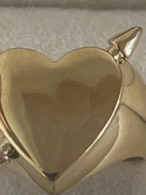 Guldfärgad ring med hjärta och pil - Cool ring i guldfärgad metall med ett stort hjärta framtill och små horn på ovansidan. Ringen har en öppen baksida vilket gör den justerbar. Perfekt för dig som gillar statement-smycken med en edgy twist. Rostfri 