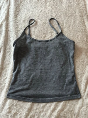 Grå linnetopp med smala axelband - En enkel och stilrena  linnetoppar med smala justerbara axelband. Toppen har en rak passform och är tillverkad i ett mjukt material som känns skönt mot huden. Perfekt att matcha med jeans eller kjol för en avslappnad look.