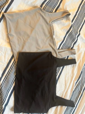 Grå/beige och svart linnetopp - Två stilrena linnetoppar i grån skiftande beige och svart med raka snitt och breda axelband. . Materialet är mjukt och stretchigt, men tyvärr okänt då lappen är avklippt på båda. Säljs tillsammans, inte för sig! Är i strl L men kan ses som lite små i storlek också.. 