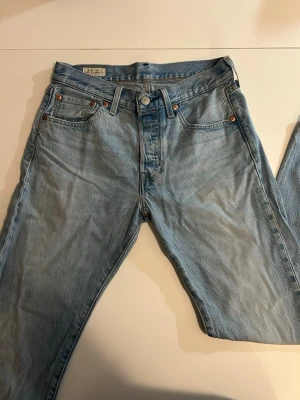 Ljusblå Levi's 501 jeans Vintage - Klassiska ljusblå Levi's 501 jeans i rak modell med fem fickor och knappgylf. Jeansen har den ikoniska läderlappen bak i midjan och röda Levi's-tag på bakfickan. Tillverkade i slitstark bomull, perfekta för en avslappnad och tidlös stil.