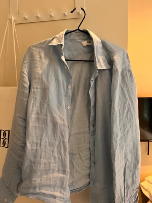 Ljusblå linneskjorta från Uniqlo - Säljer en stilren ljusblå skjorta från Uniqlo i luftigt linne. Skjortan har klassisk krage, knappar framtill och långa ärmar med knapp vid manschetten. Perfekt för en avslappnad och trendig look.