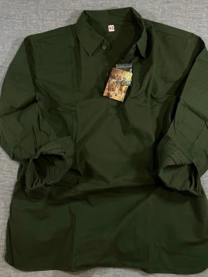 Military Olive Green Popover Field Shirt XXL (Fits XL) NWT - Pennan & Svärdet M/59 military field shirt in deep olive green. Tagged XXL (45) but fits like a relaxed XL – check measurements. Classic 3-button half-placket popover. Heavy cotton, proper field cut. Clean Scandinavian military energy. Perfect layered over tee or hoodie. Brand new with tag.  Measurements (flat): S2S 55 cm P2P 69.5 cm Waist 66.5 cm Sleeve 61.5 cm Length 86 cm 