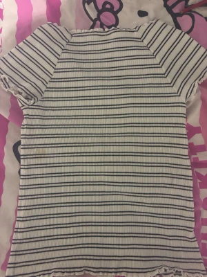 Vit ribbad t-shirt med svarta ränder - Vit ribbad t-shirt med svarta horisontella ränder och korta ärmar. T-shirten har en figurnära passform och vågiga kanter vid ärmslut och nederkant. Perfekt för en avslappnad och trendig look. Den är stretchig så den funkar också för M men den är S också 