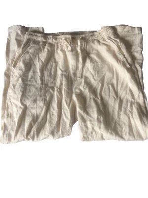 Beiga linnebyxor med resårmidja - Säljer ett par ljusbeige linnebyxor med avslappnad passform och resår i midjan. Byxorna har sidfickor fram och en bakficka med knapp. Perfekta för en chill och luftig stil under varma dagar.