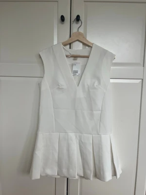 Vit kortklänning med v-ringning - student - Superfin vit klänning med V-ringning och markerad midja. Kjolen har en lätt utsvängd modell med veck som ger ett fint fall. Passar perfekt till studenten 🌸  Oanvänd med lapp kvar.  Säljer då den tyvärr inte kom till användning. Hör av dig vid frågor eller för fler bilder!