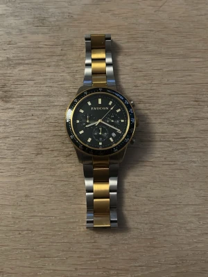 Faucon Tachymeter klocka i guld och silver - Stilren klocka från Faucon med svart urtavla, guldfärgade detaljer och tvåfärgad länk i guld och silver. Klockan har kronograf-funktion och tachymeter på ringen. Perfekt accessoar för dig som gillar en klassisk men ändå modern look. Ny pris 2800, Säljer för har fått en ny klocka och denna inte kommer till användning, vid funderingar eller frågor så hört av dig// William 