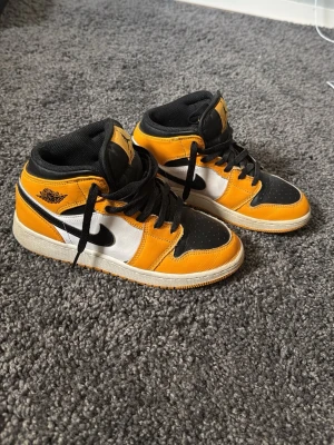 Air Jordan 1 Mid svart/gul/vit - Säljer ett par Nike Air Jordan 1 Mid sneakers i svart, gul och vit. De är väl omhändertagna, fåtal defekter synd på bilderna. Orginallåda och klistermärke tillkommer.