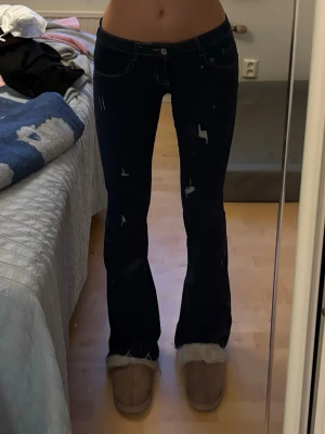 Mörkblå bootcut jeans med slitningar - Säljer ett par mörkblå bootcut jeans med snygga slitningar och låg midja. Jeansen har klassiska fickor både fram och bak samt kontrastsömmar. Perfekta för dig som gillar en trendig och avslappnad stil. Skönt material. 38 men passar mig med 36. Jag är ca 173 för referens 