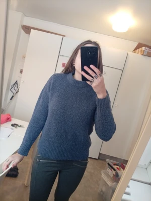 Mörkblå stickad tröja med rund hals - En enkel och snygg mörkblå stickad tröja med rund hals och långa ärmar. Tröjan har en mjuk och fluffig struktur som gör den riktigt skön att bära. Perfekt att matcha med jeans eller leggings för en avslappnad look.