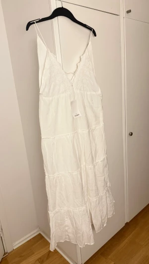 Vit sommarklänning – Storlek M från pull & bear - Oanvänd med lapp kvar. V-ringad modell med spetsdetaljer upptill och tunna axelband. Lång, luftig modell med volanger nedtill. Perfekt till sommar, semester eller festligare tillfällen. 