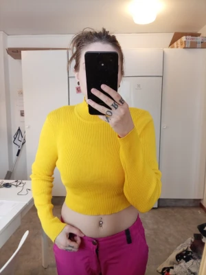 Gul ribbad croptröja med lång ärm - Säljer en snygg gul ribbad croptröja med lång ärm och hög hals. Tröjan är figurnära och har en rå kant nedtill för en trendig look. Perfekt att matcha med höga jeans eller leggings.