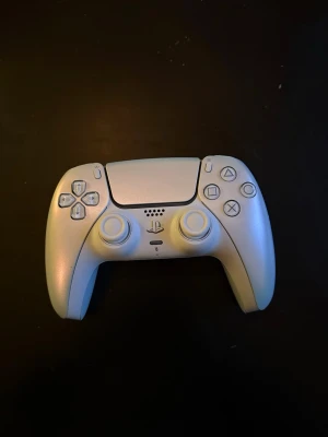  PS5 handkontroll - Snygg vit DualSense handkontroll till PlayStation 5 från Sony. Ergonomisk design med touchpad, adaptiva triggers och inbyggd högtalare. Tillverkad i plast med klassiska PlayStation-knappar och USB-C laddning. Perfekt för gaming på PS5.
