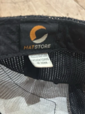 Svart truckerkeps från Hatstore - Säljer en svart truckerkeps från Hatstore med klassiskt mesh-tyg på baksidan och justerbar snapback-spänne. Kepsen har en böjd skärm och är perfekt för dig som vill ha en clean och stilren look.