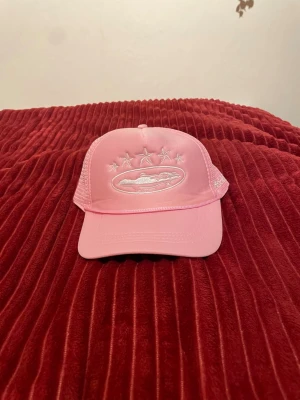 Rosa meshkeps med broderi - Säljer en snygg rosa keps med mesh på sidorna och bak, samt broderat motiv framtill med stjärnor och en bil. Justerbar baktill för perfekt passform. Perfekt accessoar för en cool och avslappnad stil.