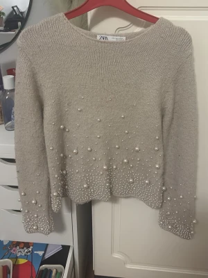 Beige stickad tröja med pärlor Zara - Supersnygg beige stickad tröja från Zara med pärldetaljer på ärmar och nedtill. Tröjan har rund halsringning och lång ärm. Perfekt för dig som vill ha något extra till din outfit. Sitter väldigt tajt i storleken så även fast den är i storlek M så passar den typ som en XS