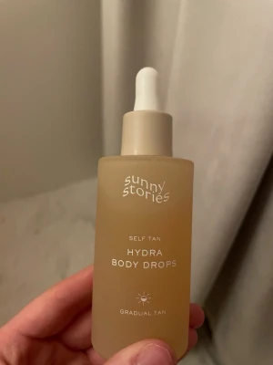 Sunny Stories Hydra Body Drops - Självbrunande droppar från Sunny Stories i en frostad beige glasflaska med pipett. Produkten heter Hydra Body Drops och ger en gradvis solbrun ton till huden. Perfekt för dig som vill ha en naturlig glow utan sol. Enkel att dosera tack vare pipetten.