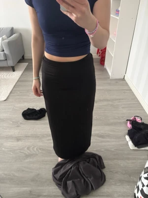 Svart långkjol med slits - Säljer en svart långkjol i stretchigt material. Kjolen har en smal passform och en snygg slits på sidan som ger extra edge till looken. Perfekt att styla med crop tops eller oversized tröjor för en trendig vibe.