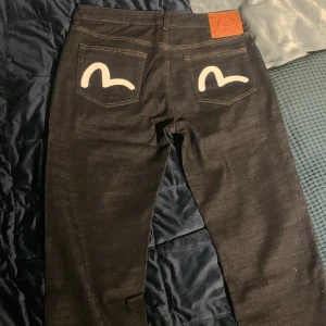 Evisu jeans med vit målad logga - Säljer ett par custom made mörkblå Evisu jeans med klassisk vit målad logga på bakfickorna. W33