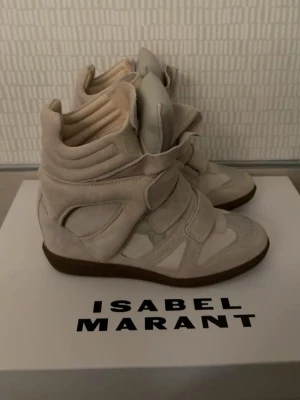 Beige Isabel Marant sneakers - Snygga beige sneakers från Isabel Marant med högt skaft och chunky design. Skorna har flera kardborreband, paneler i mocka och textil samt en brun sula. Perfekta för dig som gillar statement-sneakers med unik form och cool vibe.