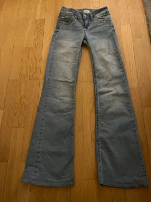 Ljusblå bootcut jeans Wrangler - Säljer ett par ljusblå bootcut jeans från Nelly med klassisk femficksdesign och snygga broderade detaljer på bakfickorna. Jeansen har normal midja och är tillverkade i mjuk denim, perfekta för en avslappnad och trendig look. Midjemått ca 33, inerbenslängs ca 74!