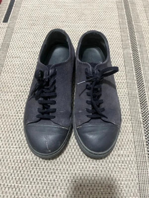 Svarta axel arigato skor - Snygga svarta sneakers med lågt skaft och klassisk design. Ovandelen är i canvas och tån är förstärkt med gummi. Skorna har svarta skosnören och en diskret sula i svart. Perfekta för en clean och enkel stil.