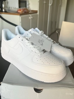 Nike Air Force 1 vita sneakers skor - Klassiska helvita Nike Air Force 1 sneakers i lågt utförande. Skorna har ovandel i slätt läder, perforerad tåbox för ventilation och Nike-logga på sidan och hälen. Tjock vit sula med AIR-dämpning för skön komfort. Perfekta för en clean och stilren look. Box is very beat up 