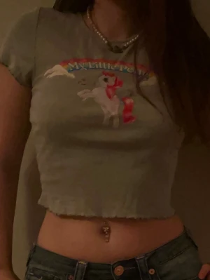 Grå croppad My Little Pony t-shirt - Grå croppad t-shirt med färgglatt My Little Pony-tryck framtill. T-shirten har korta ärmar, rund halsringning och vågig kant nertill. 