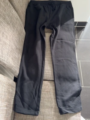 Svarta mjukisbyxor med resårmidja - Ett par klassiska svarta mjukisbyxor med rak passform och resår i midjan. Tillverkade i mjukt och bekvämt material, perfekta för chill dagar hemma eller när du vill ha det extra bekvämt. Inga synliga loggor eller detaljer.