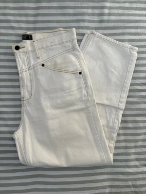 Abercrombie and Fitch Vit barrel leg jeans regular length - Säljer ett par vita jeans från Abercrombie & Fitch med raka ben och en ok-detalj framtill, samt markerade sömmar längs framsidan. Jeansen har hög midja, klassisk femfickdesign och bälteshällor. Tillverkade av tjock, icke-elastisk denim med en häftig vintage-känsla och en snygg tvätt. Ett av mina favoritpar när jag var yngre – ett riktigt häftigt och roligt par jeans för sommaren. Det finns lite gul missfärgning runt framfickan och en liten fläck på baksidan. 