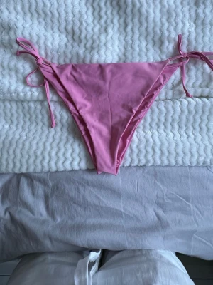 Rosa bikiniunderdel med knyt - Snygg rosa bikiniunderdel med knyt i sidorna. Klassisk trekantsmodell som ger en enkel och clean look. Perfekt för stranden eller poolen. Tillverkad i mjukt och stretchigt material för skön passform.