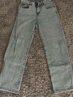 Ljusblå raka jeans från H&M - Säljer ett par ljusblå jeans med rak passform och klassisk femficksdesign. Jeansen har en knappgylf och subtila slitningar för en avslappnad look. Perfekta till sneakers eller boots för en trendig vardagsstil.