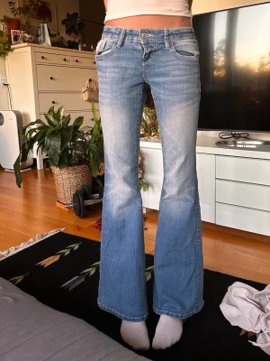 Ljusblå bootcut jeans med slitningar - Ljusblå bootcut jeans med snygga slitningar och utsvängda ben. Jeansen har klassiska fem fickor, låg midja och kontrastsömmar. Perfekta för en avslappnad och trendig look.