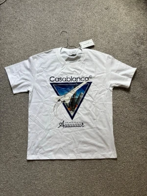 Vit Casablanca t-shirt med tryck - Snygg vit t-shirt från Casablanca med stort grafiskt tryck framtill i blått och flera färger. Klassisk passform med rund hals och korta ärmar. Perfekt statement-plagg för dig som gillar unika prints och streetstyle.