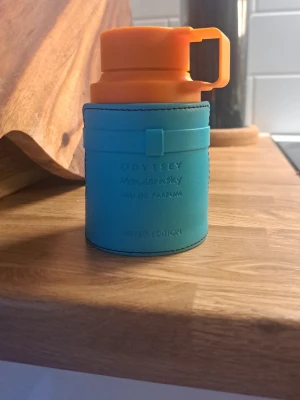 Odyssey ManLansky Eau de Parfum - Unik parfymflaska från Odyssey, ManLansky Eau de Parfum Limited Edition. Flaskan har en cool design med turkos kropp och orange lock i plast, och detaljerad söm runt om. Perfekt för dig som gillar färgstarka och moderna accessoarer.
