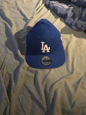Blå LA Dodgers keps från New Era - Snygg blå keps från New Era med LA Dodgers-logga framtill i vitt. Modellen är 9FORTY och har rak skärm samt justerbar passform. Perfekt för dig som gillar sportig stil och vill ha en klassisk basebollkeps.