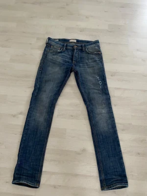 Slim Glenn jack&jones jeans - Säljer ett par blå slim fit jeans från Jeans Intelligence, modell Slim Glenn. Jeansen har slitna detaljer, klassisk femficksdesign och är tillverkade i bomull med lite stretch. Snygg tvätt och smal passform som sitter skönt längs benen. Jeansen är i toppskick (slutningarna är detaljer). Skriv för minsta fundering så hjälper jag dig. Jeansens storlek är W28 L32