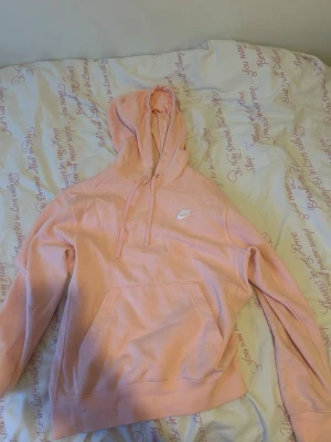 Ljusrosa hoodie från Nike - Säljer en ljusrosa hoodie från Nike med klassisk huva och dragsnören. Tröjan har en stor magficka framtill och Nike-logga broderad i vitt på bröstet. Perfekt för en avslappnad och sportig stil. Använd en gång.