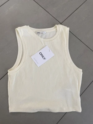 Ribbad vit croppad linnetopp ONLY - Säljer en helt ny  vit croppad linnetopp från ONLY. Fått i present men var för stor för mig. Toppen är ärmlös med rund halsringning och har en clean, enkel design som passar perfekt till jeans eller kjol. Materialet är mjukt och stretchigt för en bekväm passform. Skriv för frågor!🤍