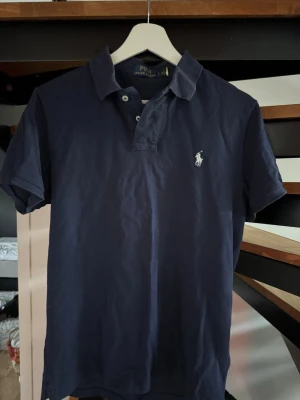 Ralph Lauren pike - Marinblå Ralph Lauren pike i strl S. En snygg marinblå raffe piké i väldigt bra skicka, perfekt nu på sommaren. Hör av er vid funderingar!