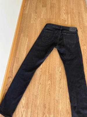 Svarta Lee jeans med raka ben - Säljer ett par svarta jeans från Lee med klassisk femficksmodell och raka ben. Jeansen har Lee-logga på bakfickan och är tillverkade i ett slitstarkt denimtyg. Perfekta för dig som gillar en tidlös och enkel stil. Storlek 31&32 det är inga konstigheter med dem, har använt dem någon gång
