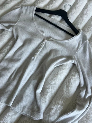 Grå ribbad långärmad topp från Brandy Melville - Säljer en grå ribbad långärmad topp med rund halsringning och knappar framtill. Toppen har en slim passform och är tillverkad i mjuk bomull, perfekt att styla till olika outfits. Jag är villig att diskutera priset🤍