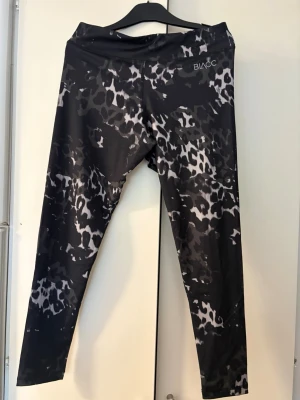 Svarta leopardmönstrade tights från BLACC - Snygga svarta träningstights från BLACC med leopardmönster i grått och vitt. Tillverkade i stretchigt syntetmaterial som passar perfekt för träning. Hög midja och åtsittande passform för en sportig look.