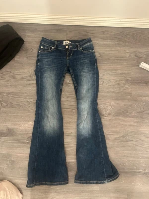 Blå bootcut jeans från 157 - Snygga blå bootcut jeans från 157 med klassisk femficksdesign och ljusa slitningar framtill. Jeansen har låg midja och utsvängda ben, perfekt för en avslappnad och trendig look. Materialet är klassisk denim i bomull. (Använda bara en gång) köpte de för 400