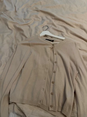 Beige kofta från lager 157 - Stilren beige kofta från 157 med rund halsringning och knappar framtill. Aldrig använd och är i storlek S